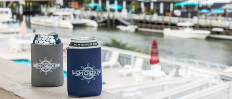 Two beverage containers with the Shem Creek Inn logo on a dock overlooking a marina with boats and buildings in the background.