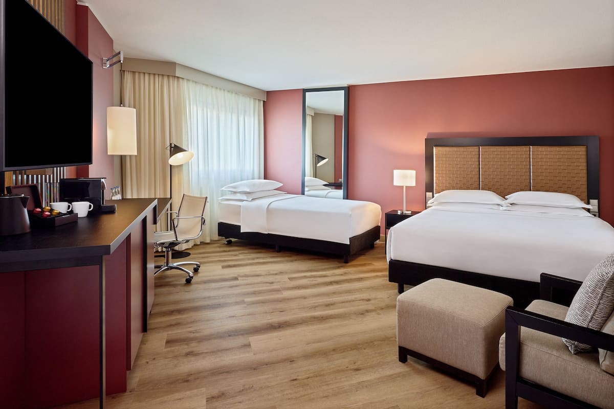 A hotel room with two beds, a desk, a chair, a TV, and a large mirror.