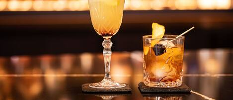 Deux verres d’une boisson sont posés sur le comptoir d’un bar, avec un arrière-plan flou composé de bouteilles.