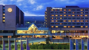Un hotel Sheraton con diseño moderno, que presenta un logotipo destacado y varios pisos con ventanas iluminadas.