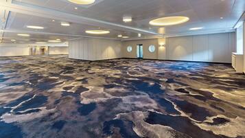 A spacious room with a patterned carpet, recessed ceiling lights, and a door leading to another area.