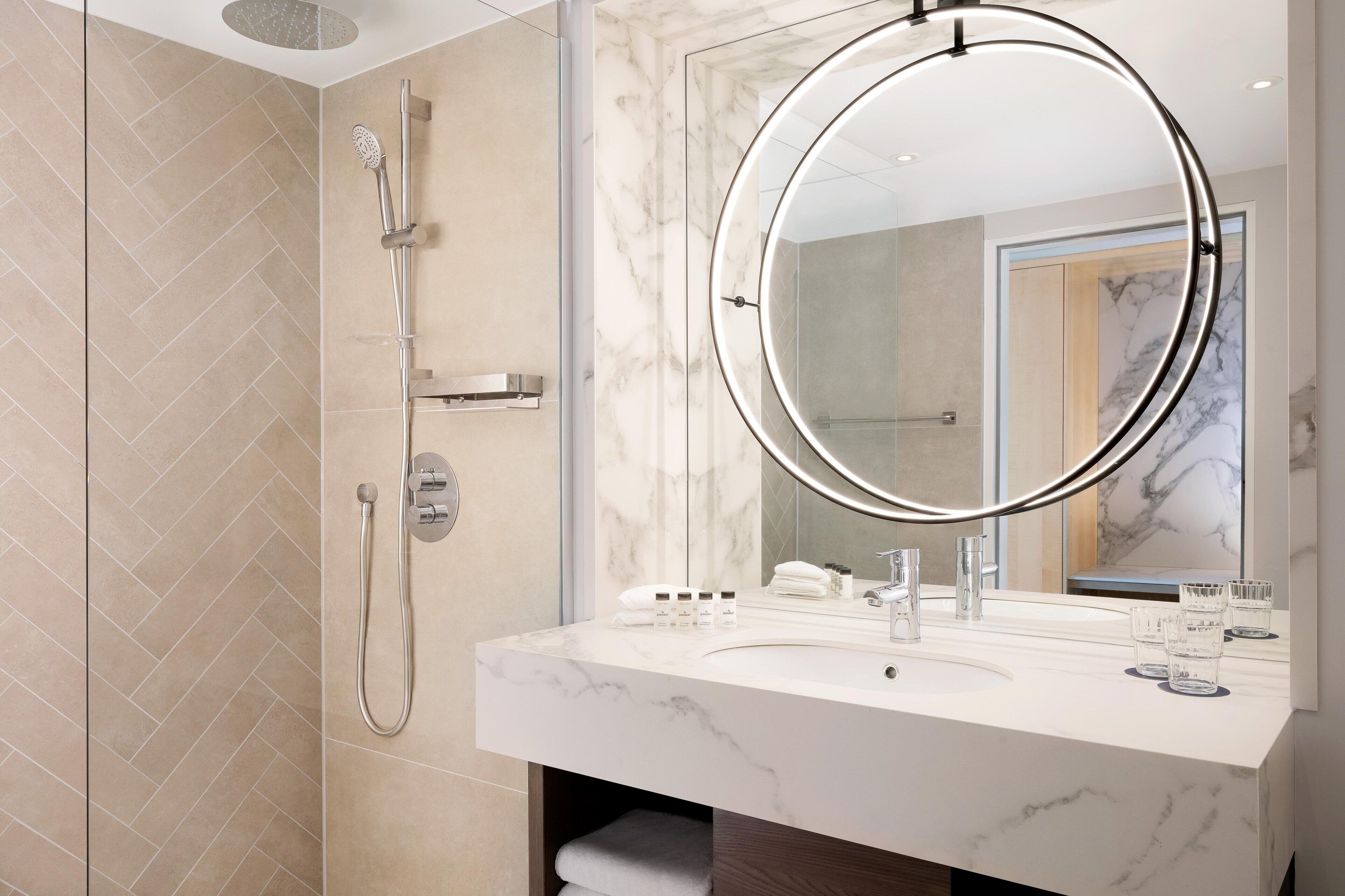 A modern bathroom with a large mirror, a shower, and a marble countertop.
