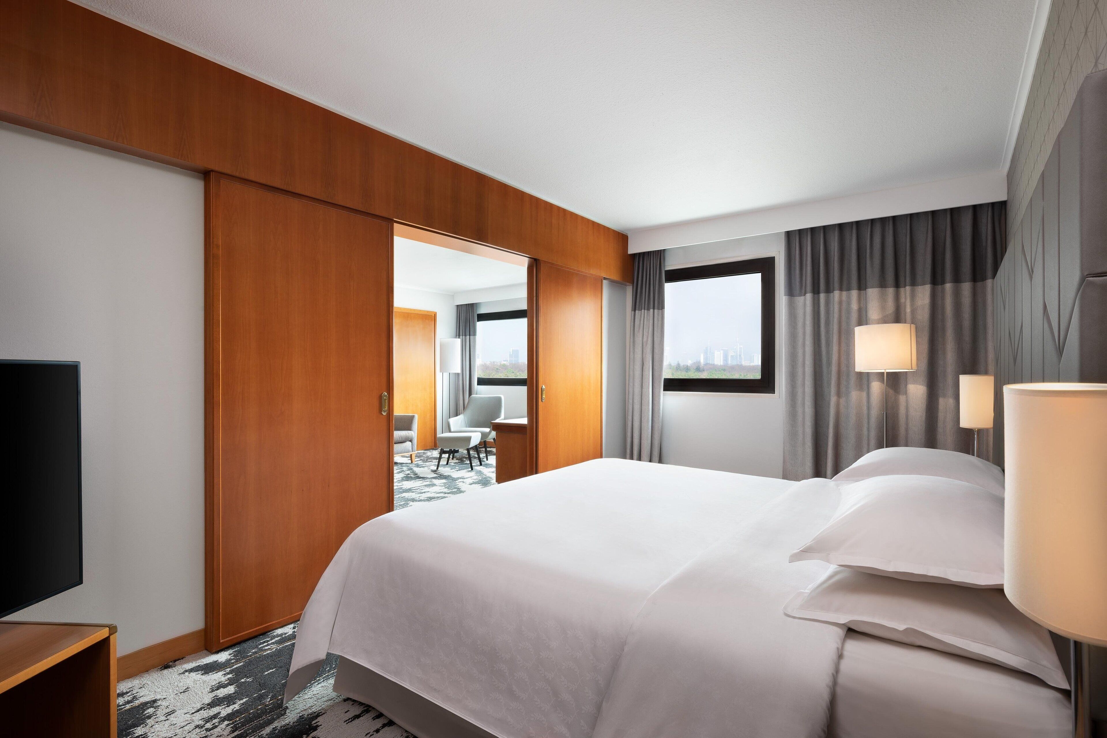Habitación de hotel con cama, televisión, escritorio, silla y vista a la ciudad.