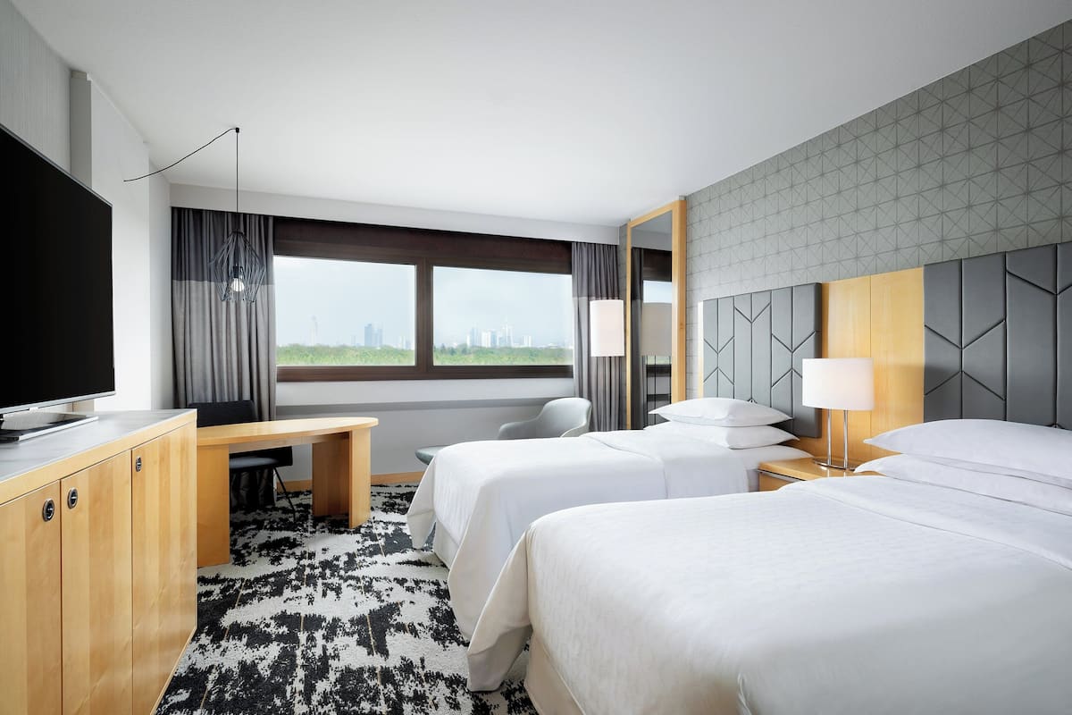 A modern hotel room with a large bed, a desk, a television, and a city view.
