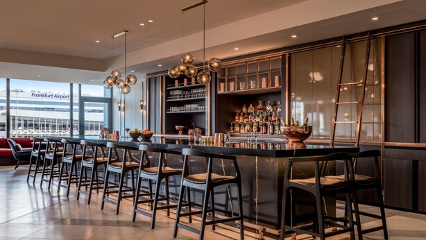 Un área de bar moderna con una barra larga, varios taburetes y una amplia variedad de botellas y vasos.