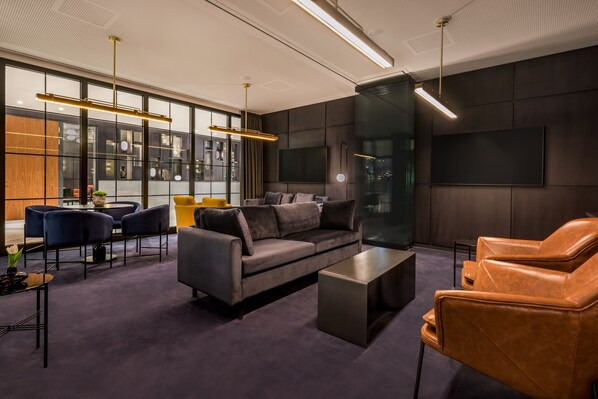 A modern living room with a sofa, armchair, and coffee table, large windows, and a flat-screen TV.