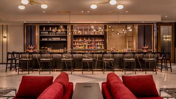 A bar area with a long counter, multiple chairs, and a seating area with red sofas.