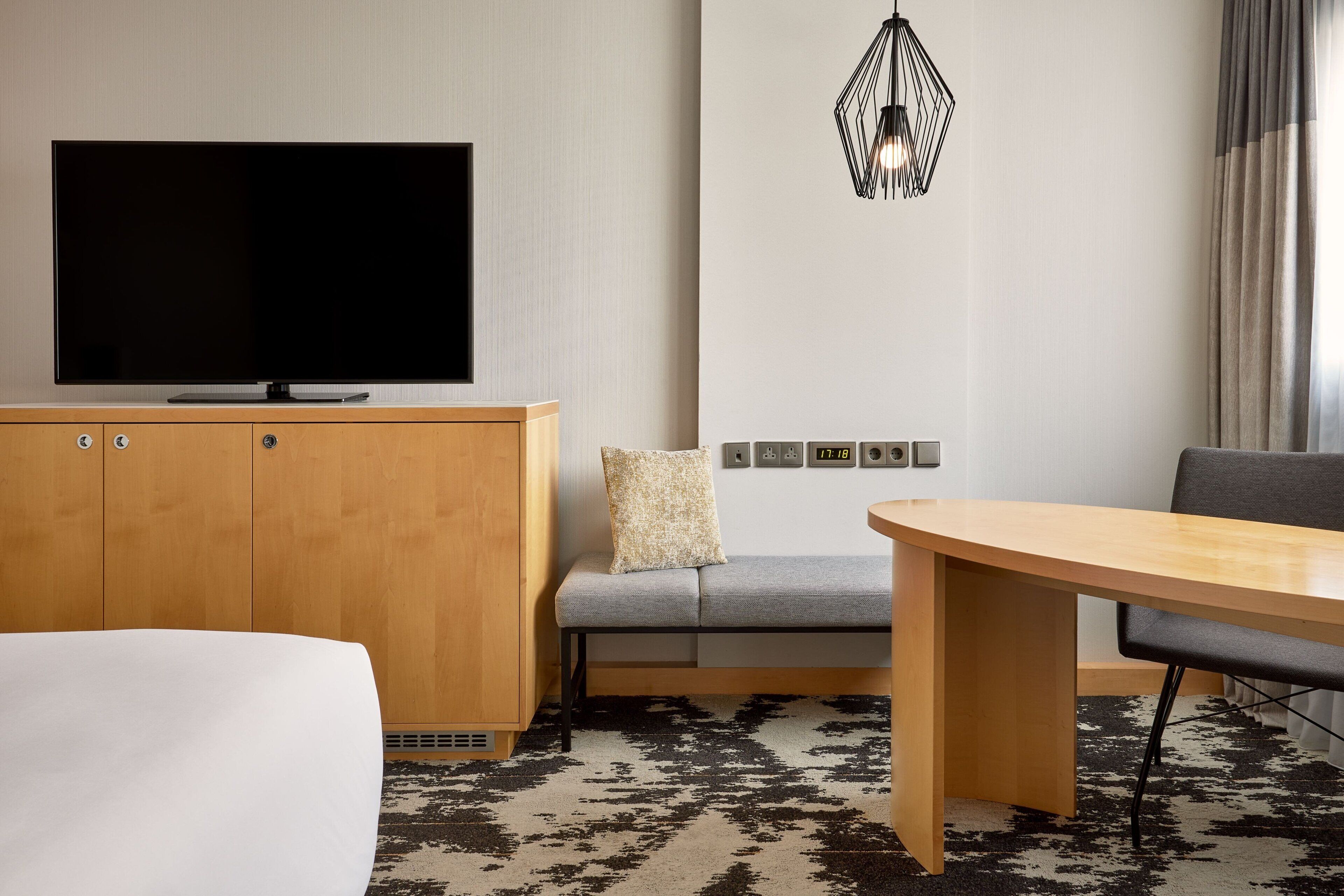 Hotelkamer met flatscreen televisie, een bank, een eettafel en een kamerbreed tapijt met dessin.