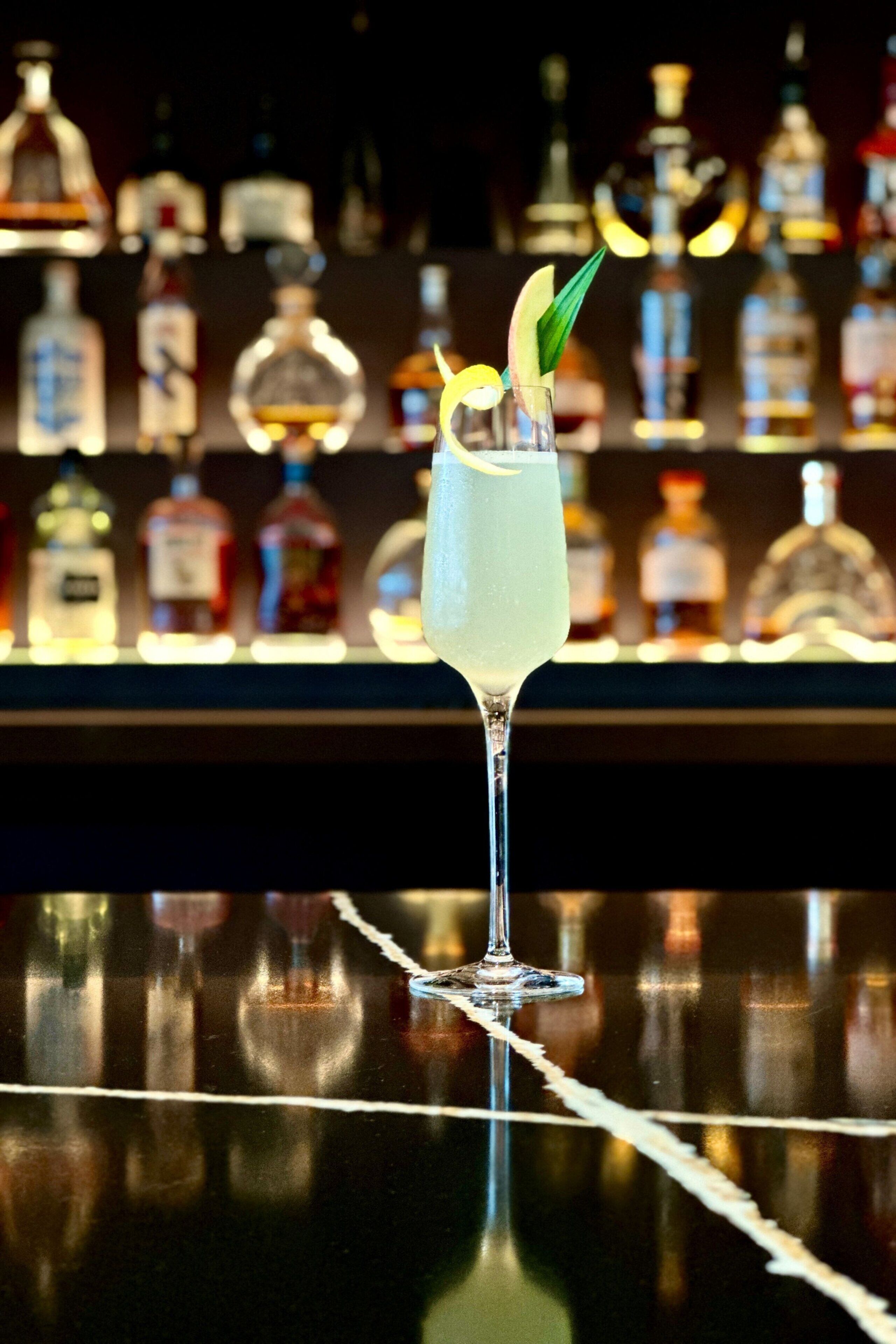 A bar setting with a clear glass containing a beverage, a bar counter, and a background of various bottles.
