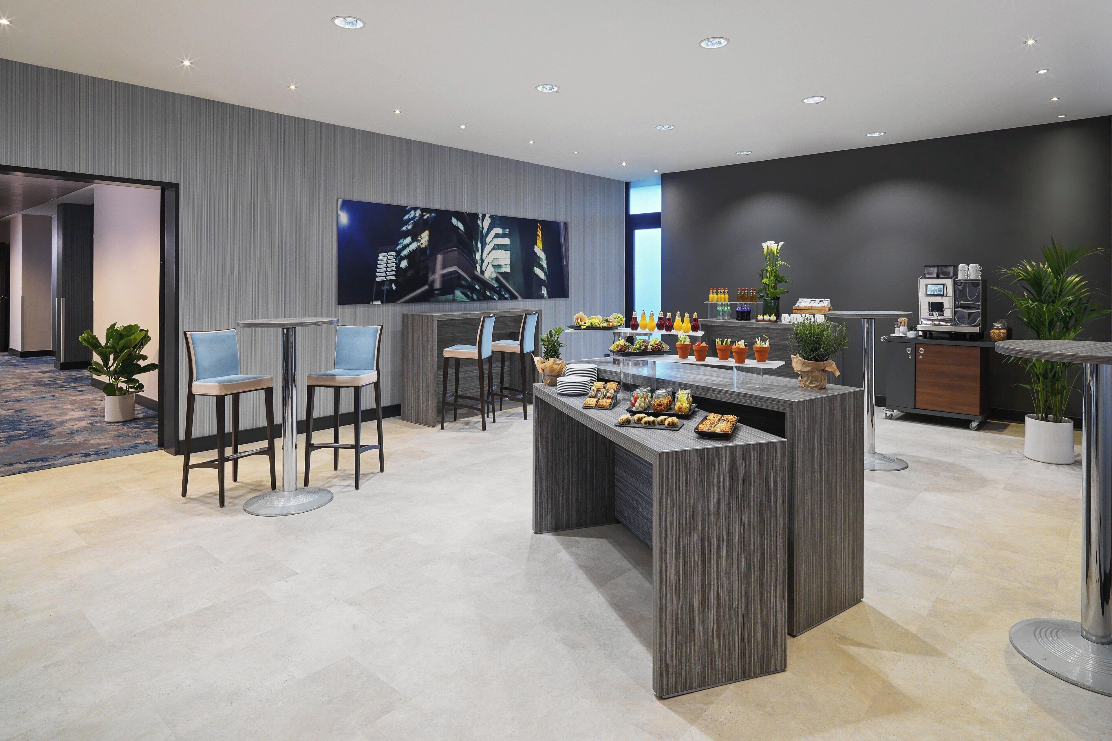 Un hall d’hôtel moderne avec un comptoir d’accueil, un espace salon et un grand tableau représentant un paysage urbain accroché au mur.