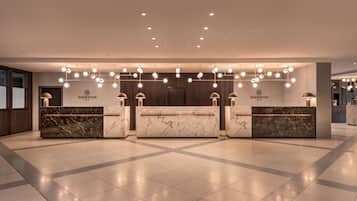A hotel reception area with marble reception desks, overhead lighting, and a modern design.