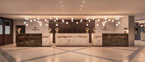A hotel reception area with marble reception desks, overhead lighting, and a modern design.