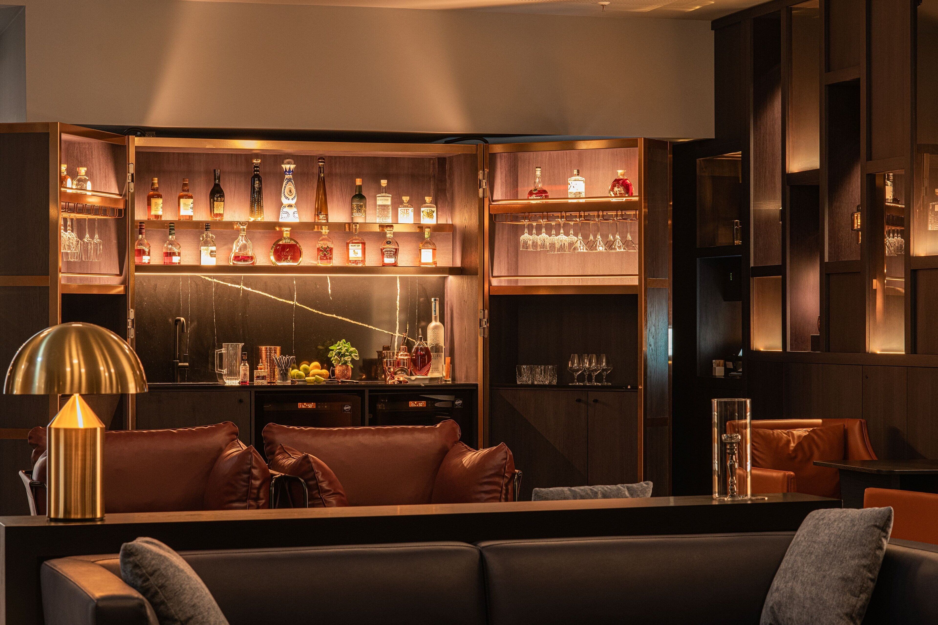 A bar area with multiple shelves of bottles and glasses, a bar counter, and leather seating.