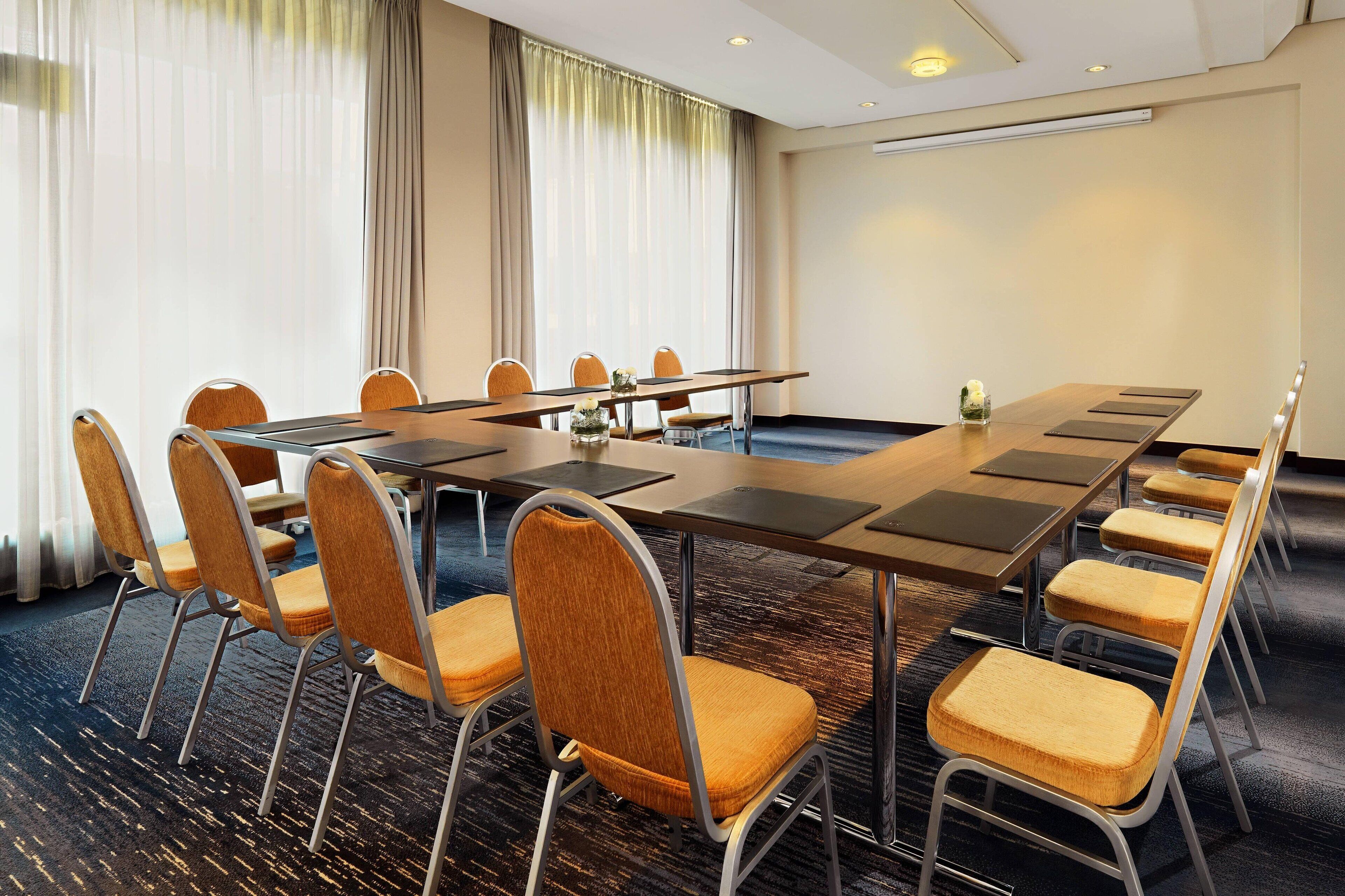 Un salón de conferencias con una larga mesa, varias sillas y piso alfombrado.