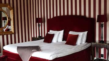 A large bed with white linens and red pillows, a gold-framed mirror, and striped wallpaper.
