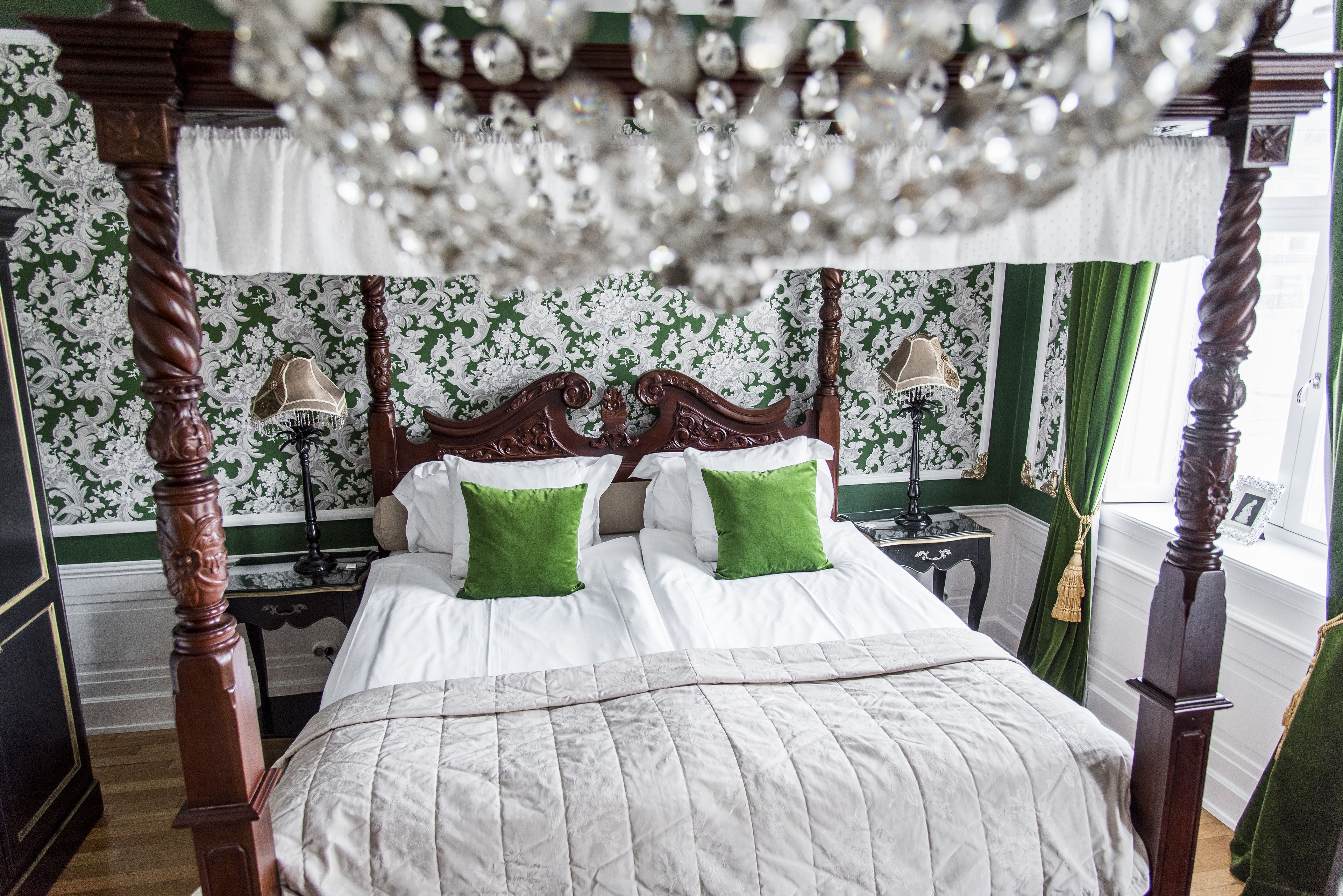 Una cama con dosel y cuatro columnas con ropa de cama verde y blanca, un candelabro y un fondo de papel tapiz floral.