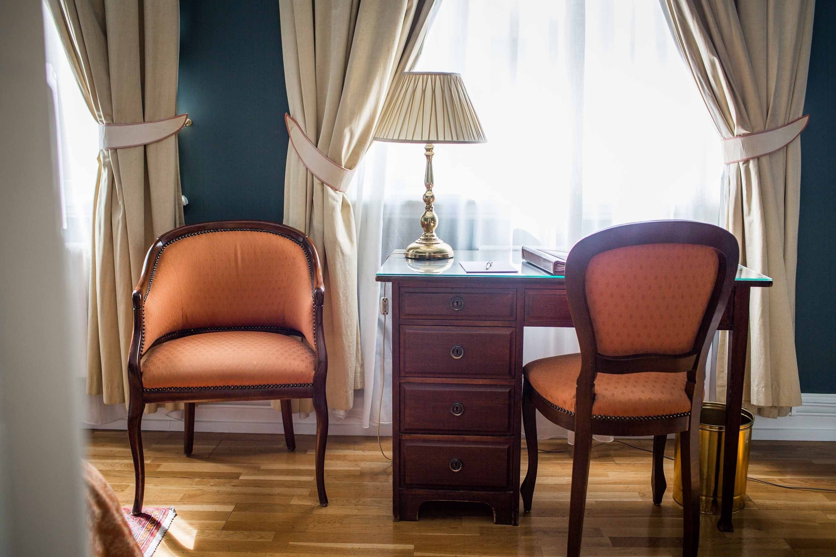 Una habitación con dos sillas, un escritorio, una lámpara y una ventana con cortinas.