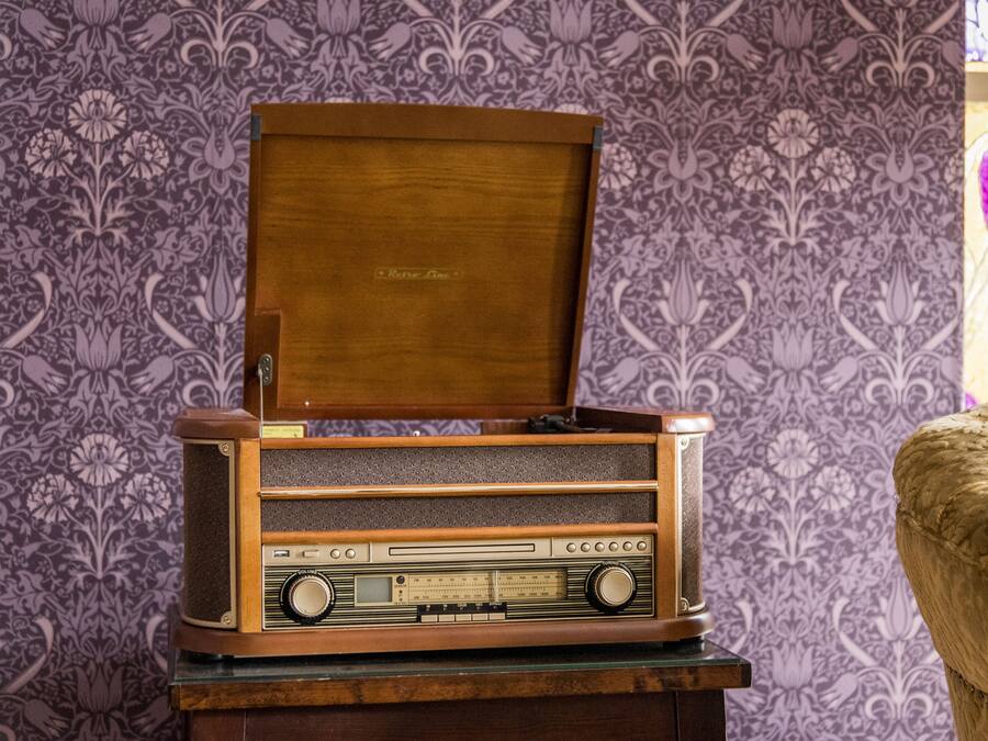 En gammal radio placerad på ett träställ, med en tapet med mönster som bakgrund.