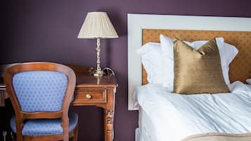 A hotel room with a bed, a wooden nightstand, a lamp, and a blue upholstered chair.