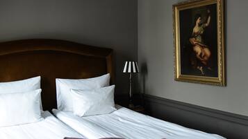 Una cama bien hecha con sábanas y almohadas blancas, un cabecero de madera, una lámpara con pantalla a rayas y un cuadro en la pared.