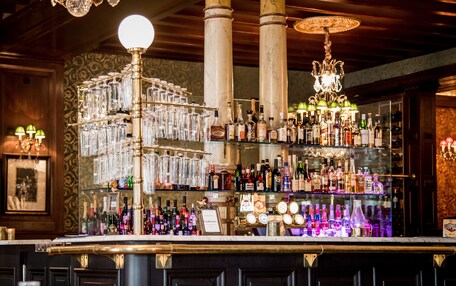A bar area with a glassware display, shelves of liquor bottles, and decorative lighting.