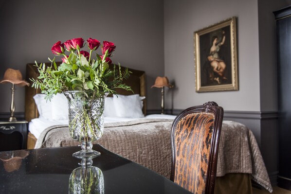 Un dormitorio con una cama, una mesita de noche, una lámpara, una silla y un florero con flores.