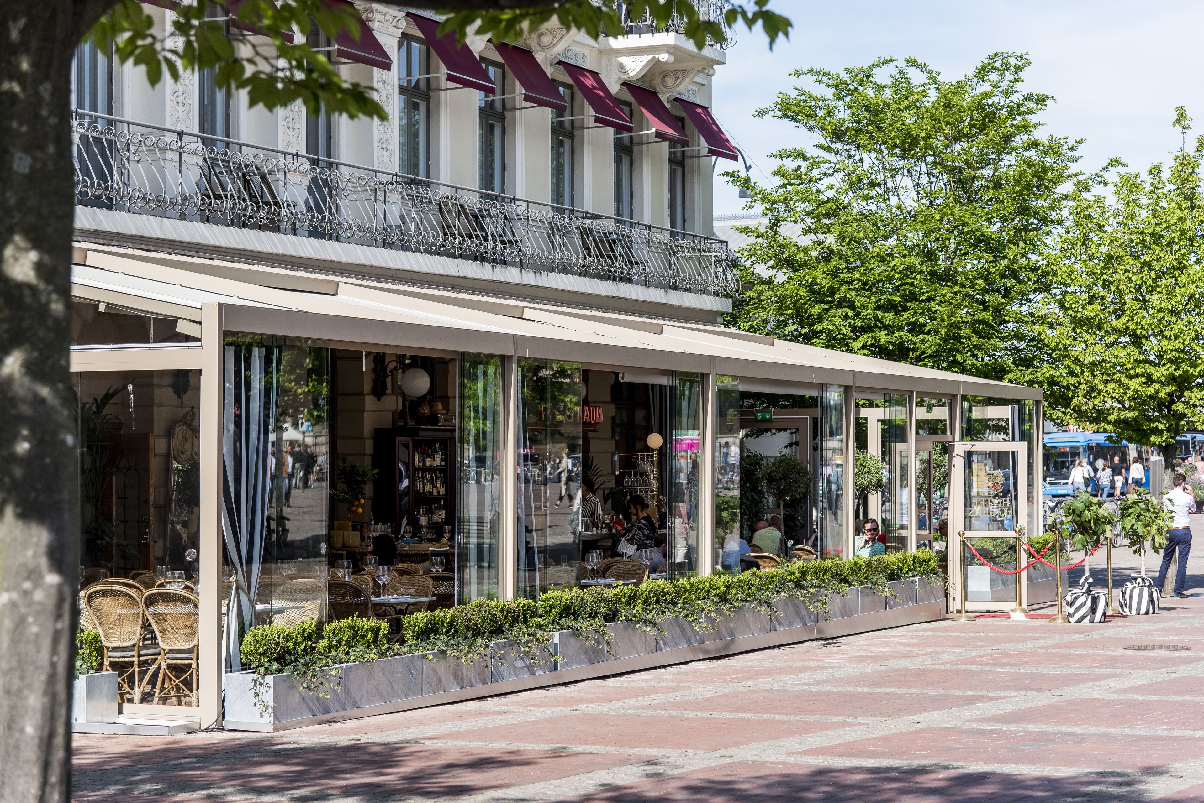 A cafe with outdoor seating, large windows, and a balcony with decorative railings.