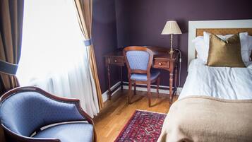 A hotel room with a bed, a desk with a chair, a lamp, and a patterned rug.
