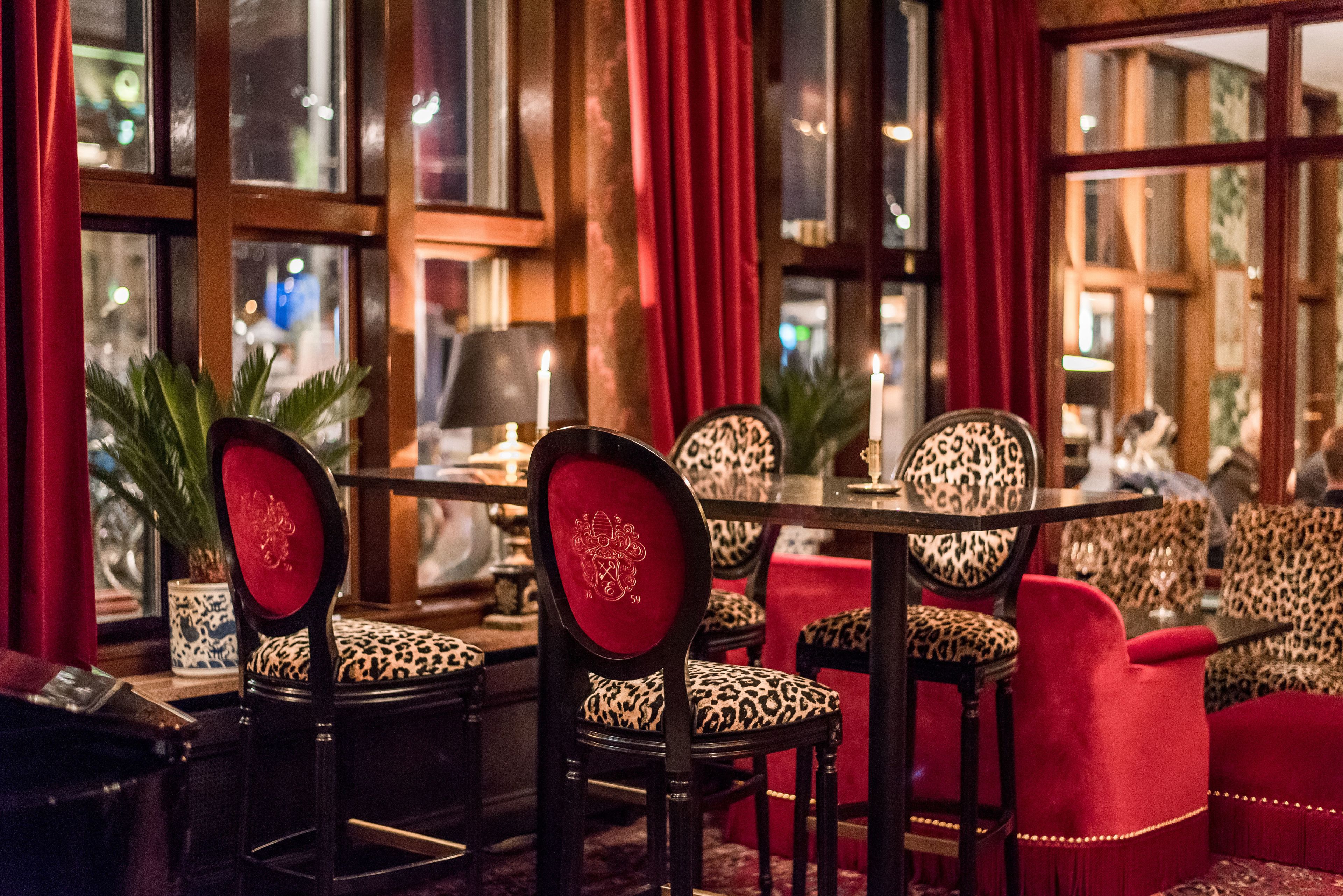 A dining area with red curtains, leopard print chairs, and a table with candles.