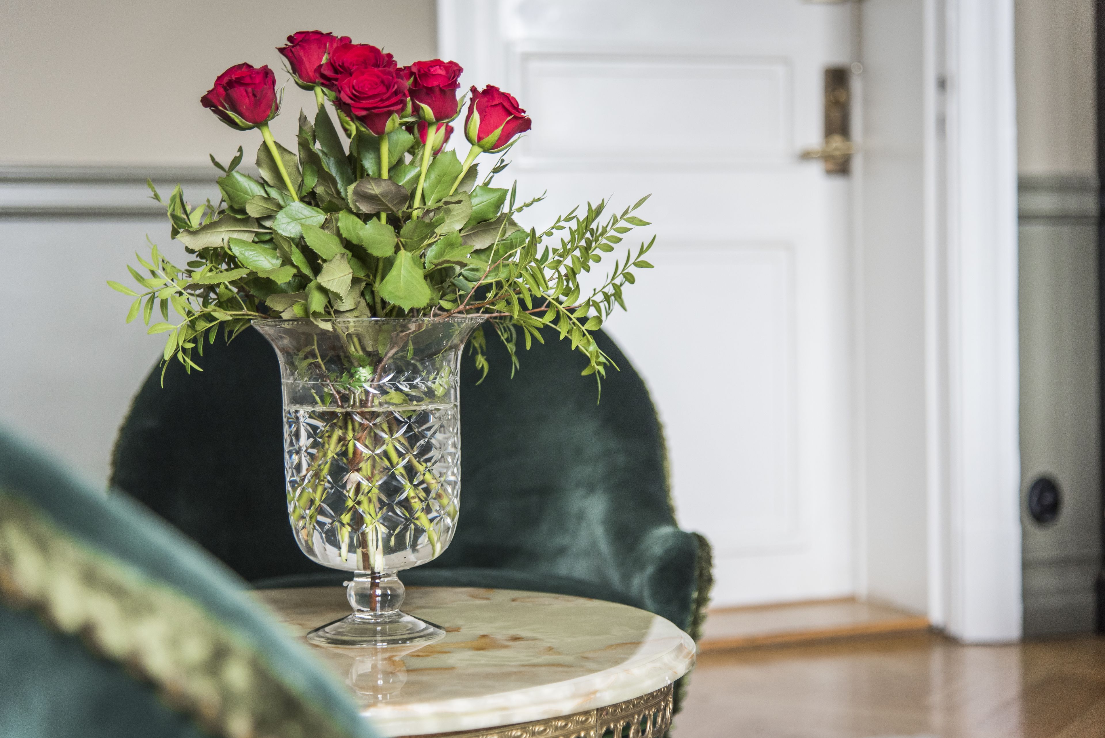 A clear glass vase with red roses and green foliage on a marble table.