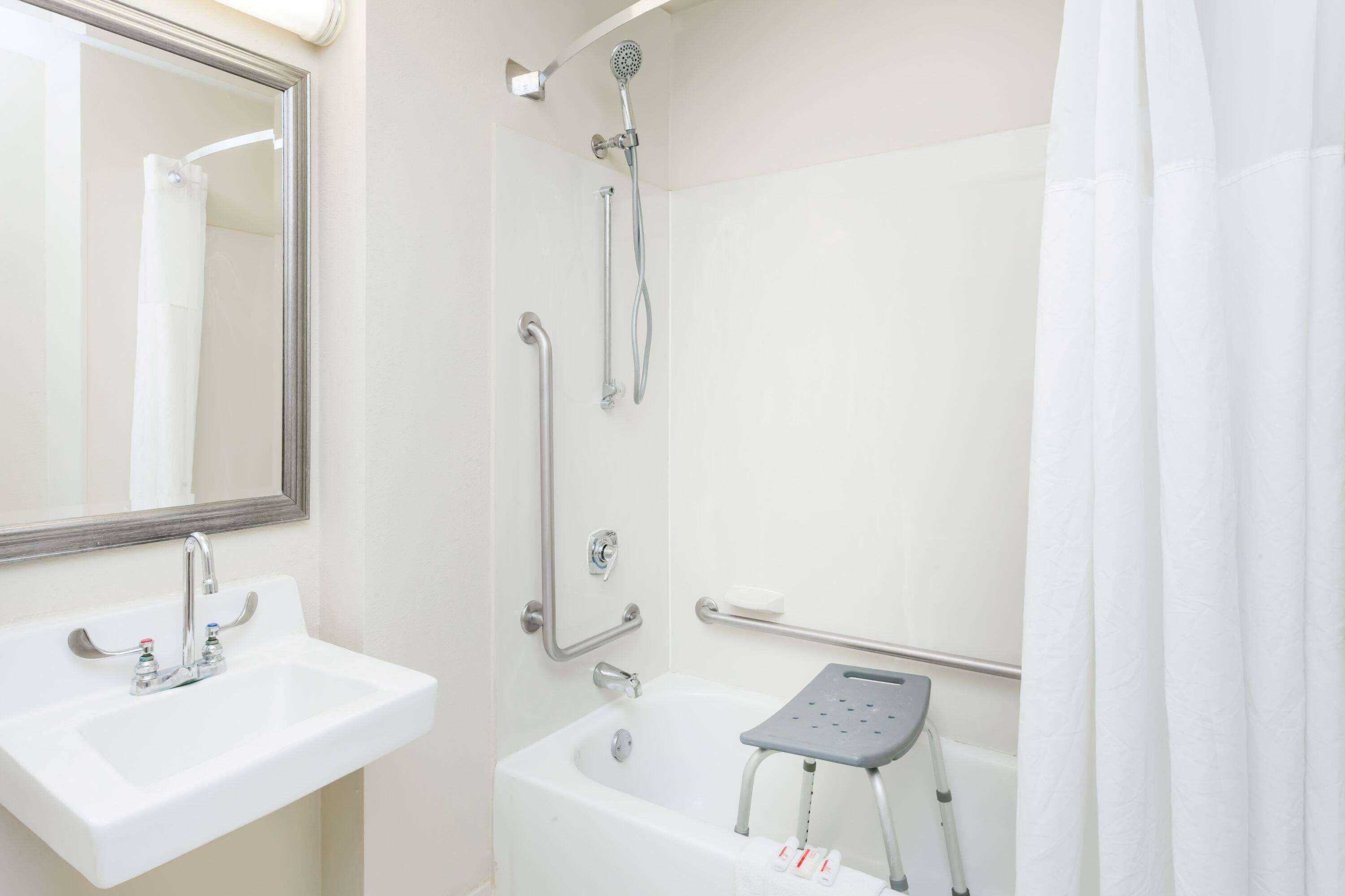 A bathroom with a sink, mirror, shower, and grab bars.