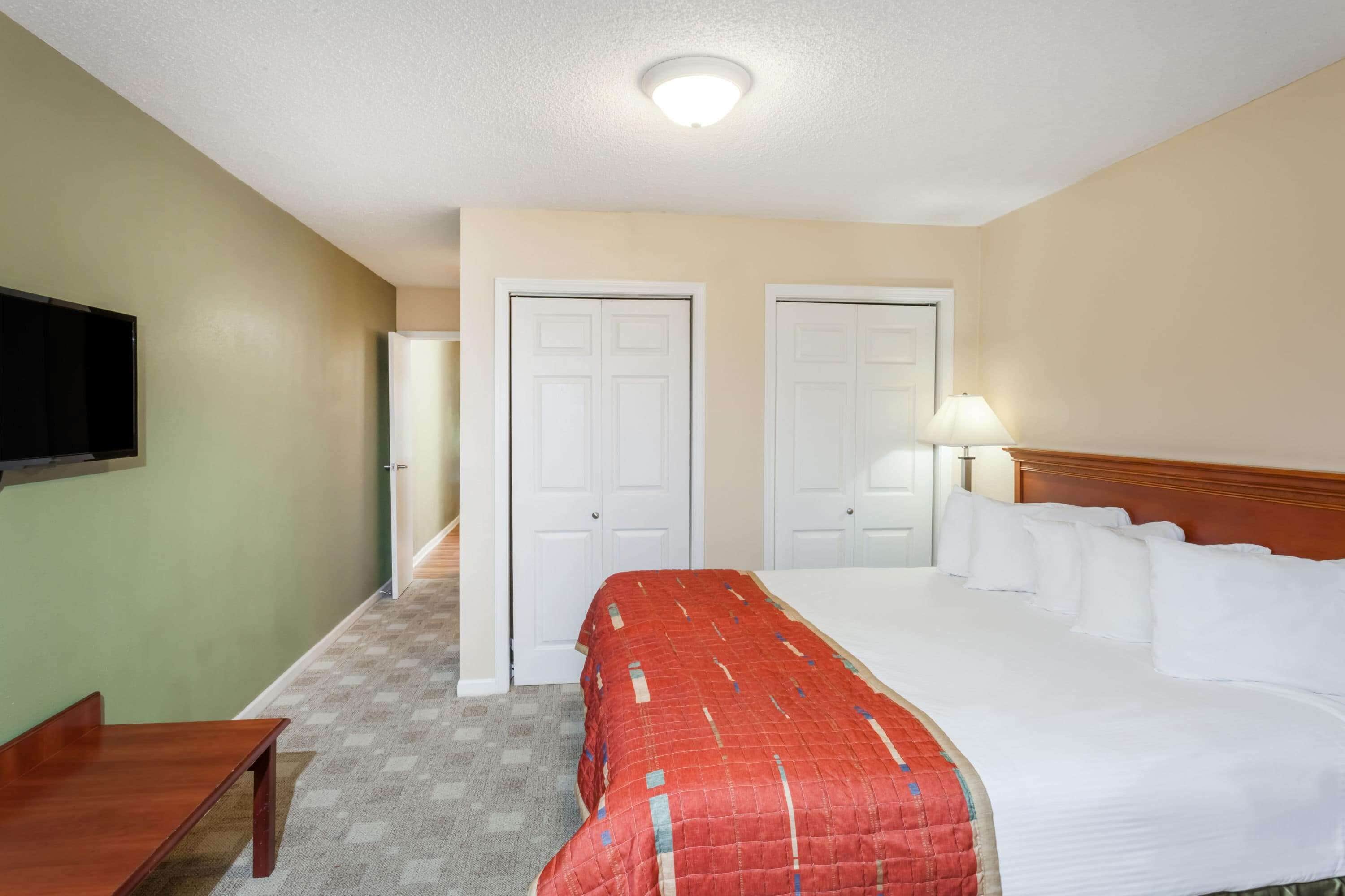 Una habitación de hotel con una cama grande, un escritorio, un televisor montado en la pared y dos puertas.