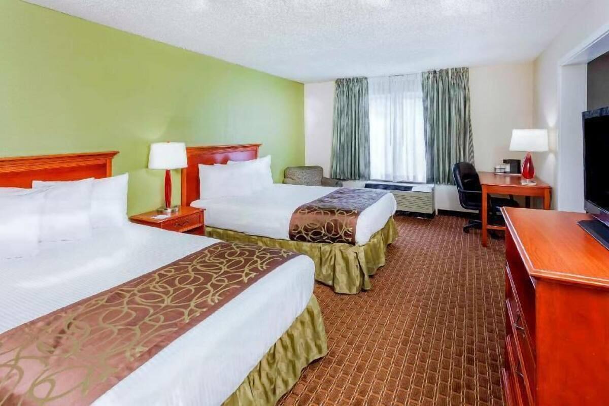 A hotel room with two beds, a desk, a television, and a window with curtains.