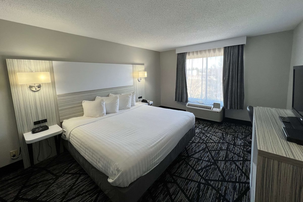 Een hotelkamer met een groot bed, nachtkastjes, een bureau en een raam met gordijnen.