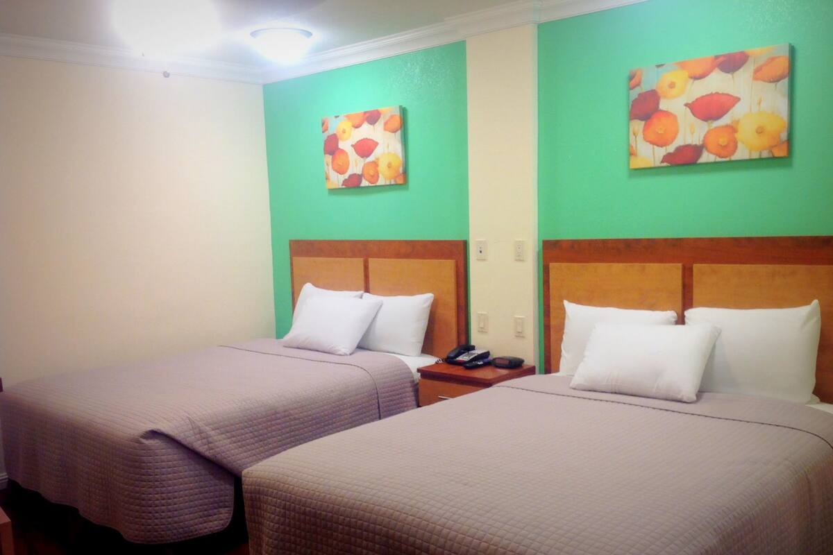 A hotel room with two beds, each with a wooden headboard and white bedding. There are two paintings on the walls, one above each bed.
