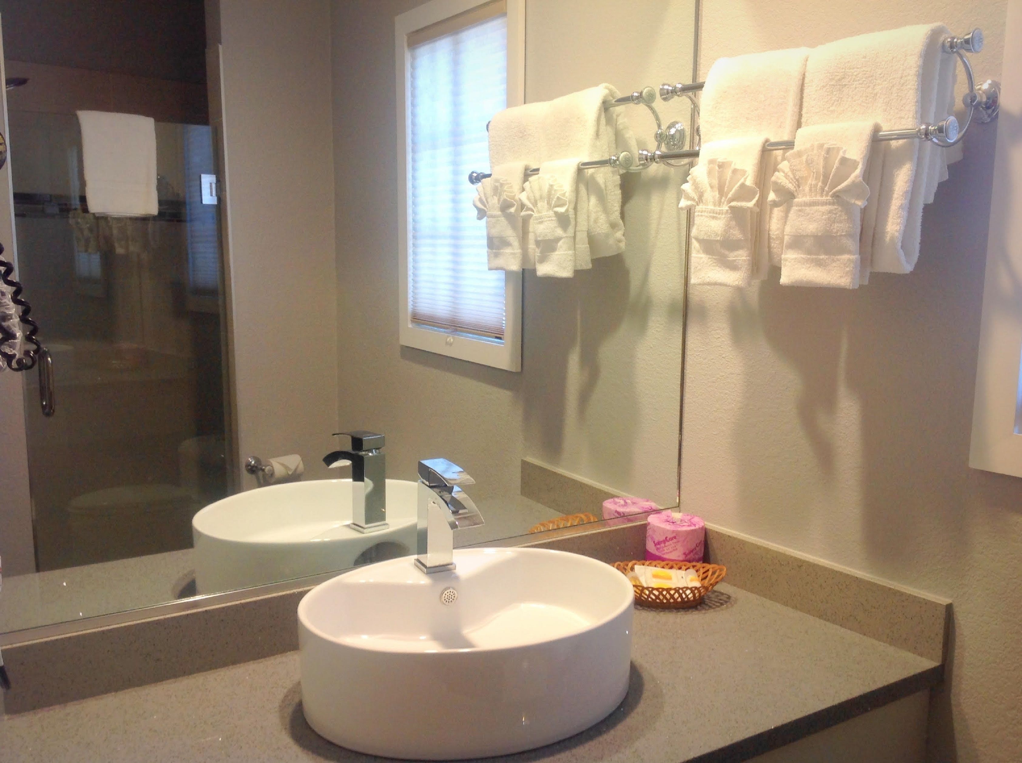 Un baño con dos lavamanos, un espejo y un perchero con varias toallas.