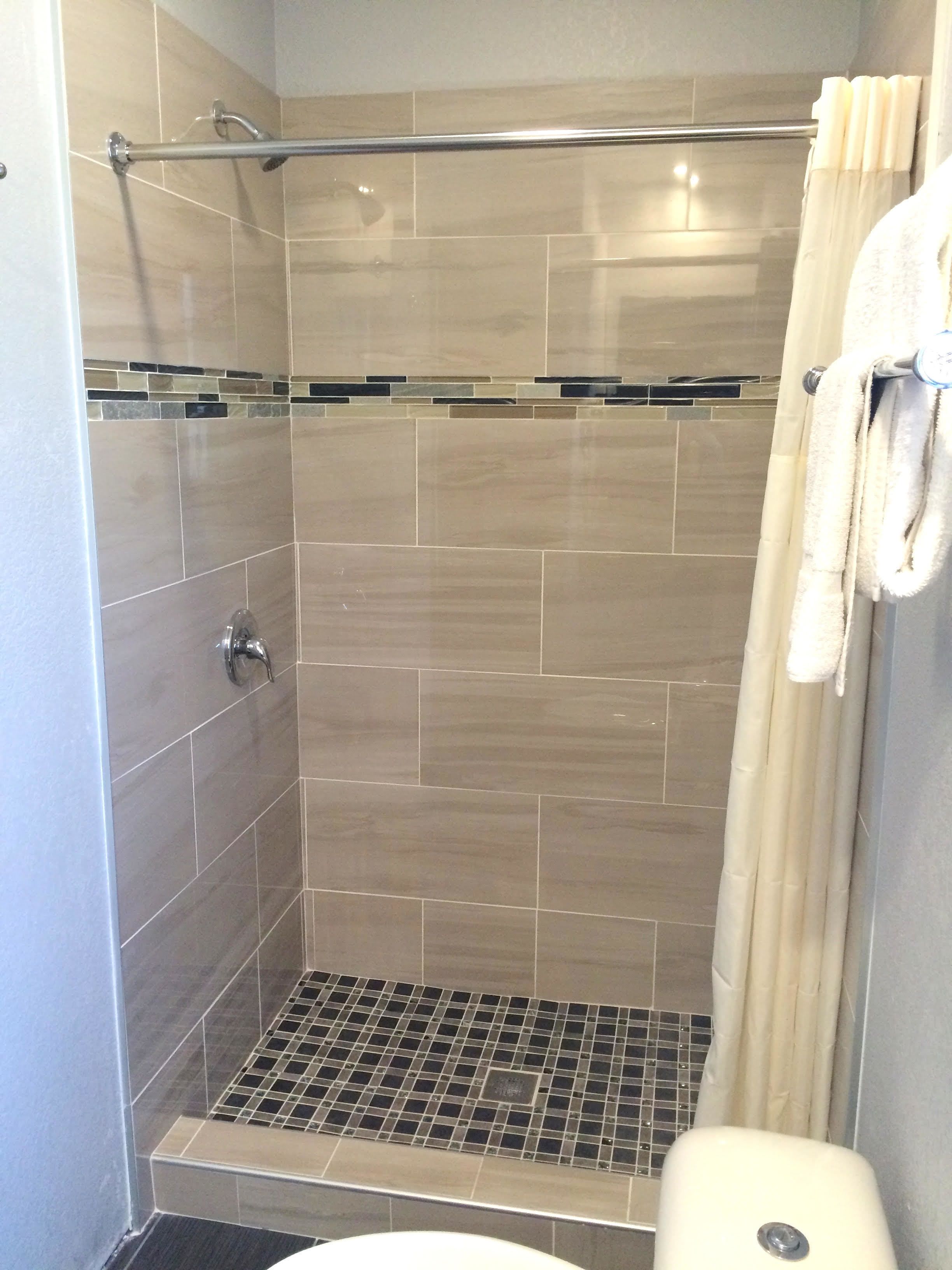 A shower area with a glass door, a metal grab bar, and a tiled floor.