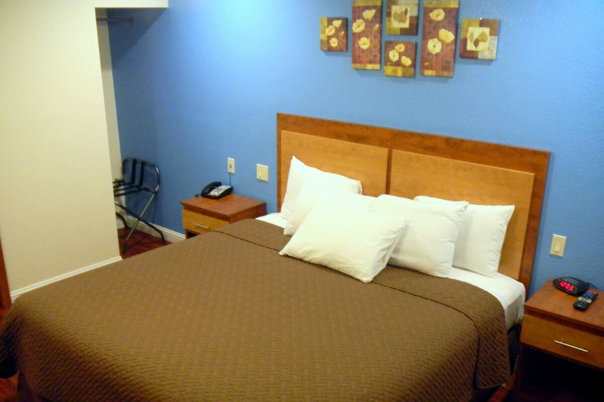 A hotel room with a large bed, a wooden headboard, a bedside table with a phone, and a wall with artwork.