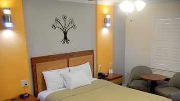 Habitación de hotel con cama, mesitas de noche, una silla, una mesita pequeña y un adorno en la pared.