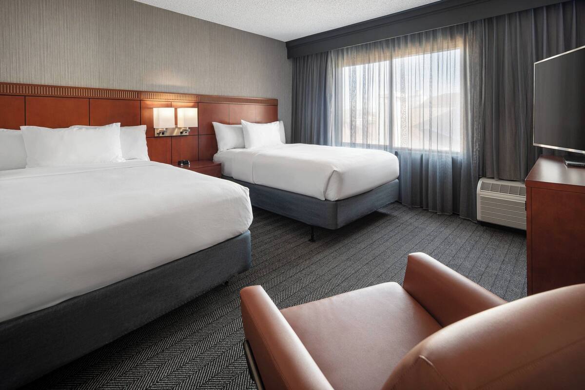 A hotel room with two beds, a desk, a chair, and a large window with curtains.