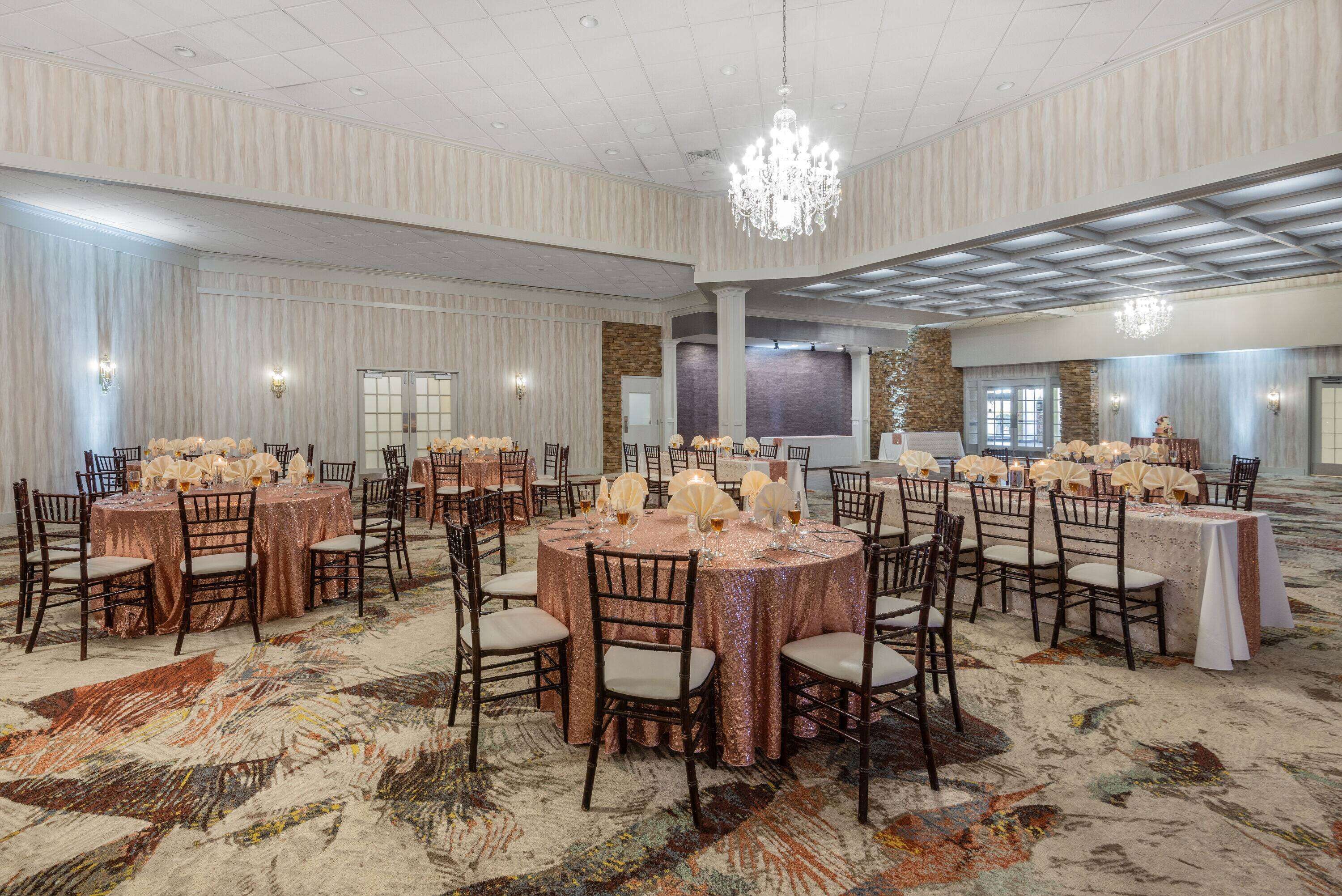 A large banquet hall with round tables set for events, featuring a patterned carpet and elegant chandeliers.