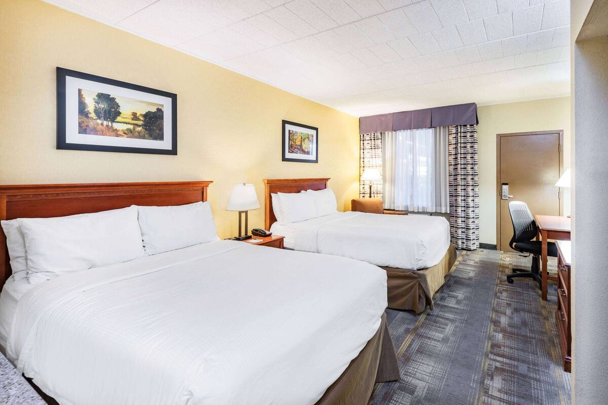 Une chambre d’hôtel avec deux lits, un bureau, une chaise et deux tableaux encadrés au mur.