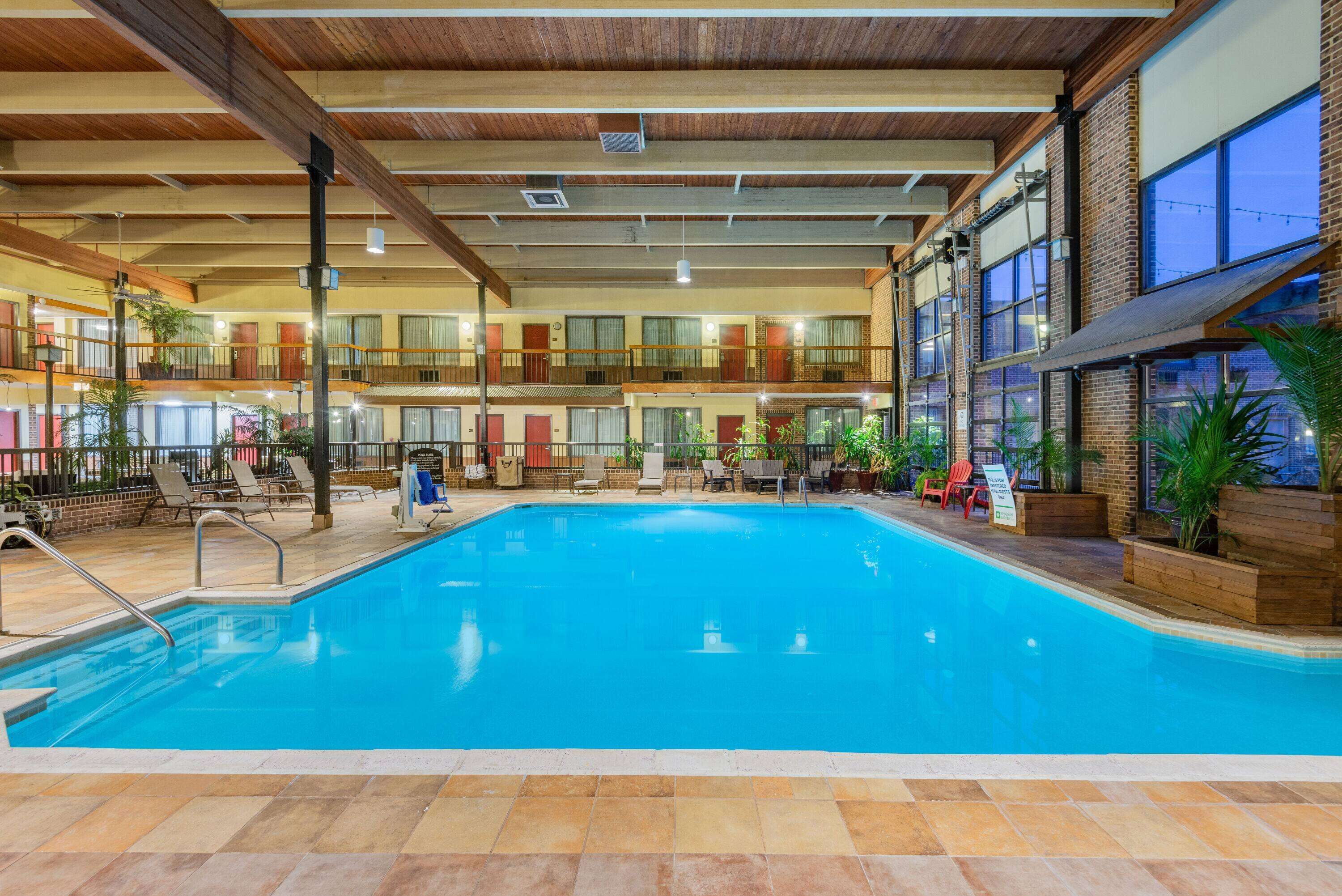 Una piscina interior con varios niveles de balcones, sillones de descanso y plantas en macetas.