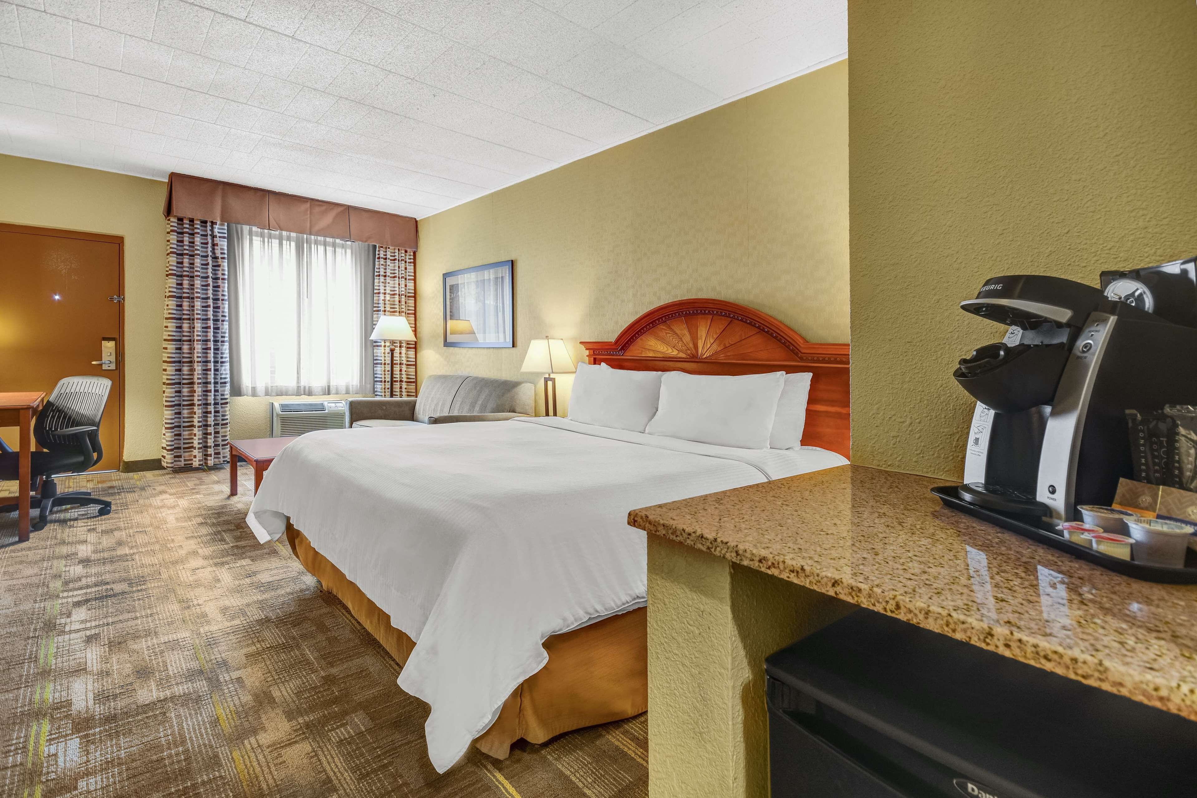Una habitación de hotel con cama, escritorio, silla y cafetera.