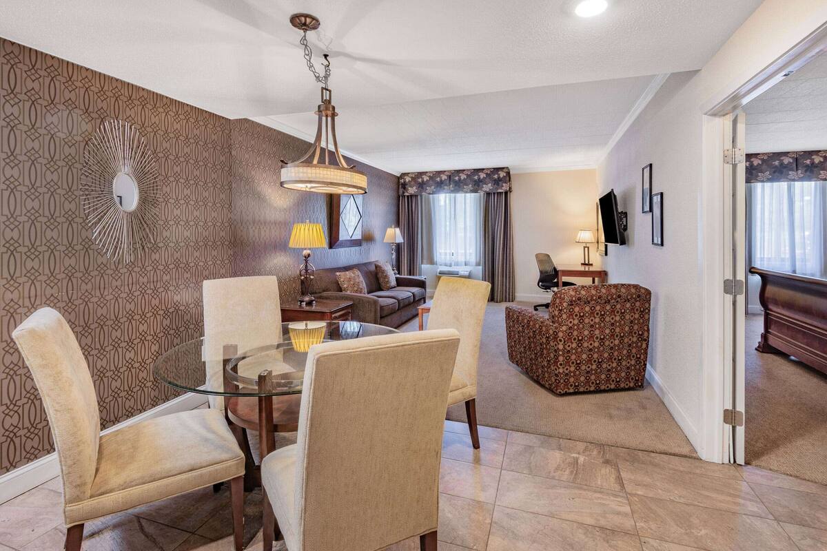 Un salon moderne avec une table basse en verre, des fauteuils recouverts d’un tissu beige, un canapé à motifs et un pouf à motifs.