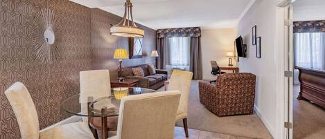 A modern living room with a glass coffee table, beige upholstered chairs, a patterned sofa, and a patterned ottoman.