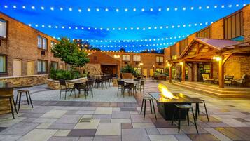 Un patio al aire libre con edificios de ladrillo, mobiliario exterior e iluminación con guirnaldas.