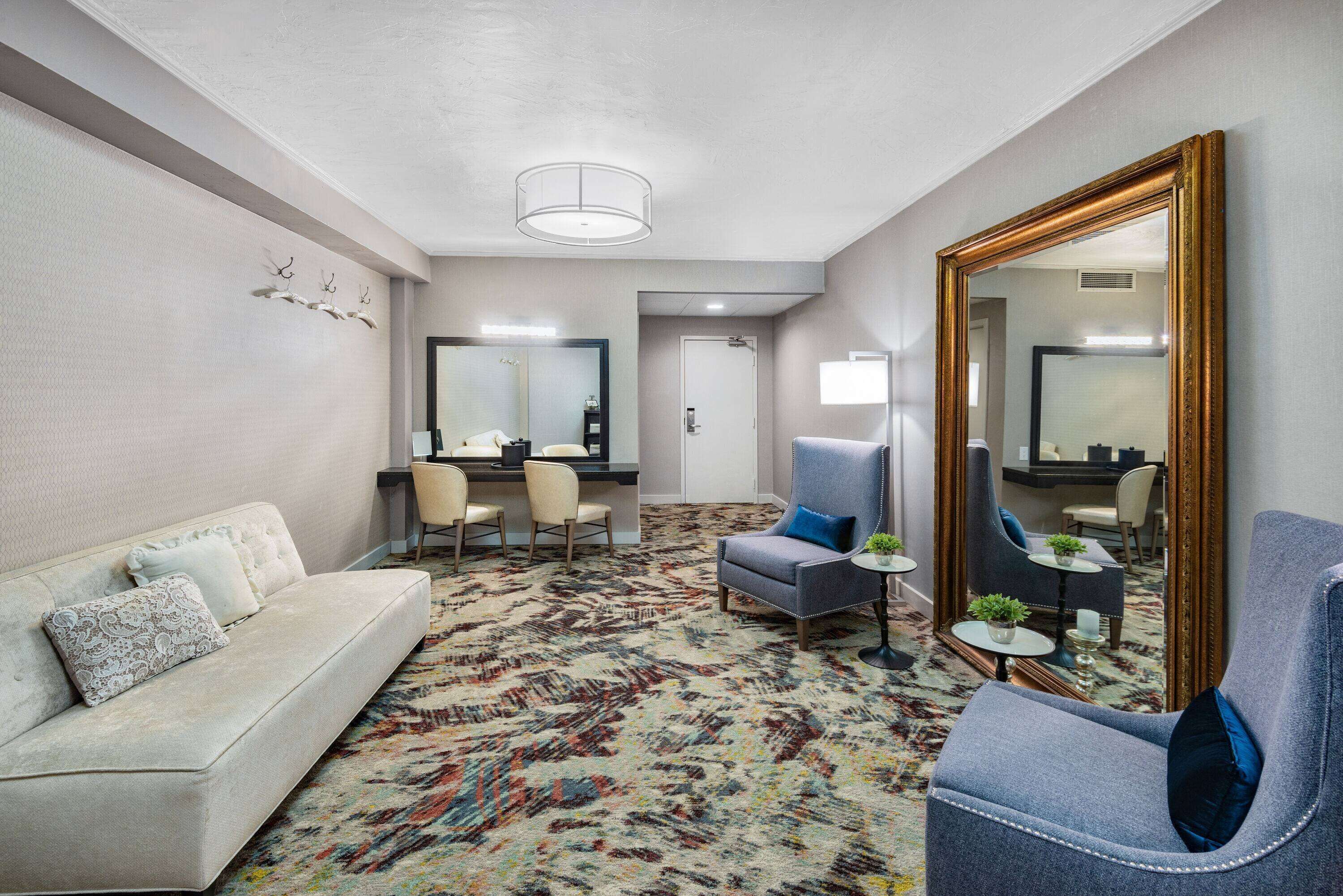 A hotel room with a sofa, armchairs, a desk, and a large mirror.