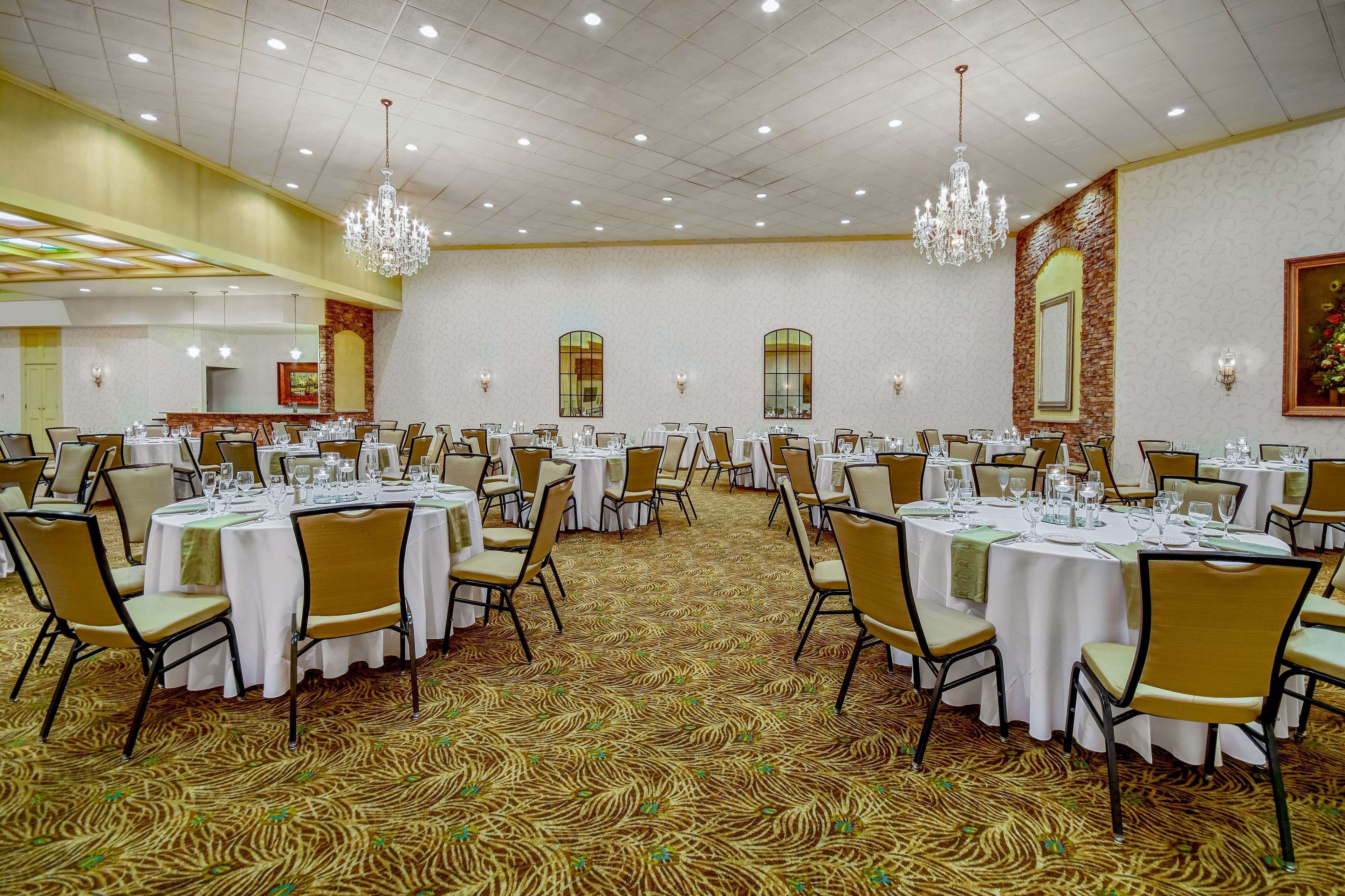 Un salón de banquetes con mesas redondas, sillas, candelabros y alfombra estampada.