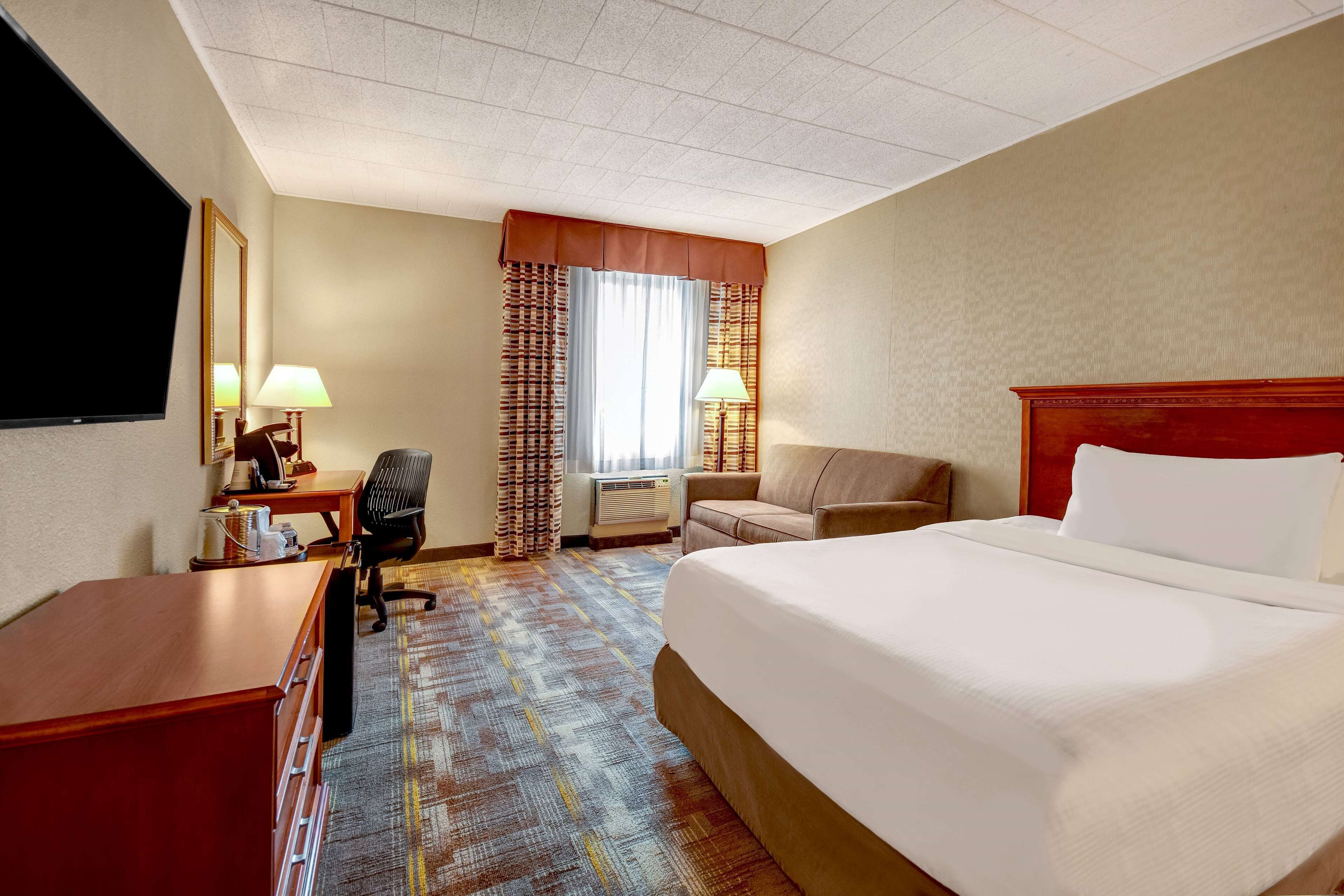 A hotel room with a large bed, a desk with a chair, a TV, and a window with curtains.